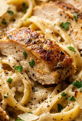 Ultra close-up macro food photograph of creamy garlic parmesan chicken pasta with golden seared chicken and fettuccine